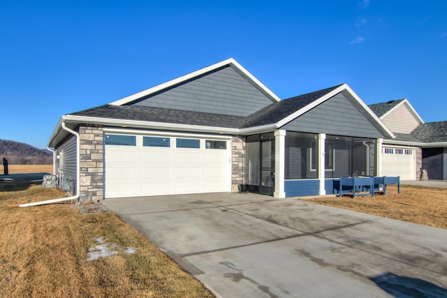 view of front of home featuring an attached garage, a sunroom, stone siding, driveway, and a front lawn