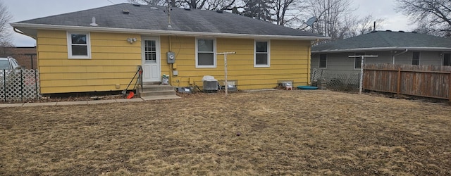 rear view of house with entry steps, fence, and roof with shingles