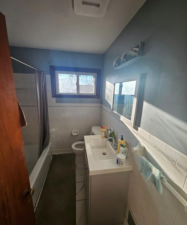 bathroom featuring tile walls, toilet, shower / bath combo with shower curtain, wainscoting, and vanity