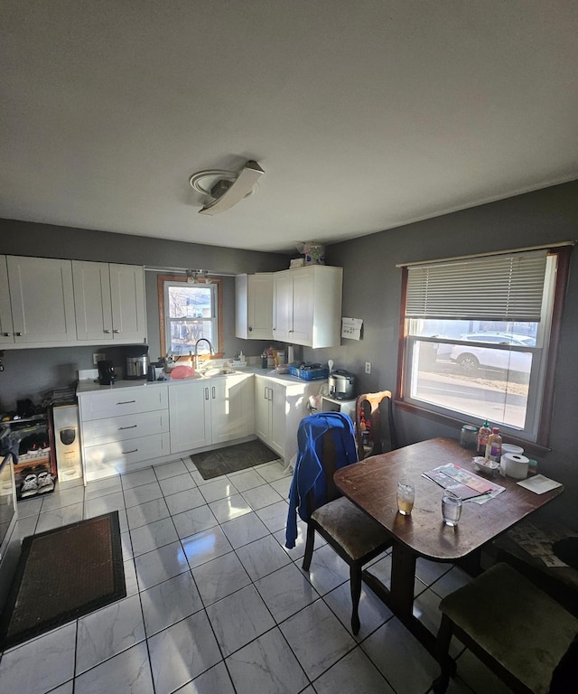 kitchen with marble finish floor, white cabinets, a sink, and light countertops