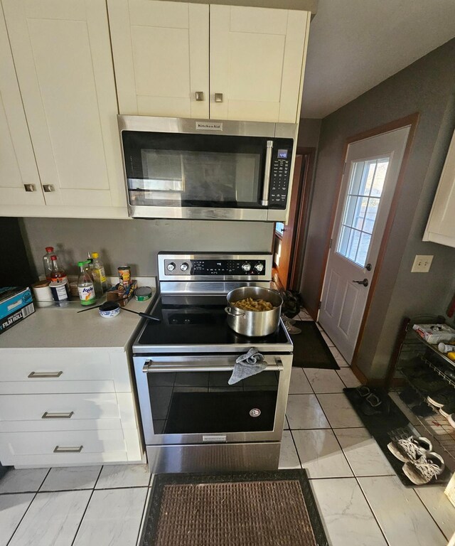 kitchen with appliances with stainless steel finishes, light countertops, marble finish floor, and white cabinets