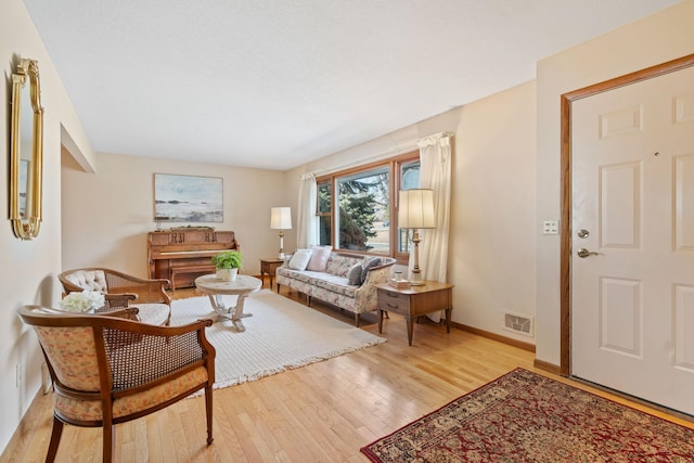 living room featuring light wood-type flooring, visible vents, and baseboards