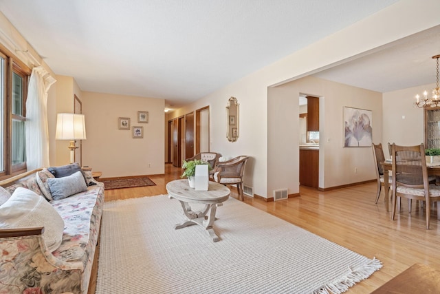 living area featuring visible vents, light wood-style flooring, baseboards, and an inviting chandelier