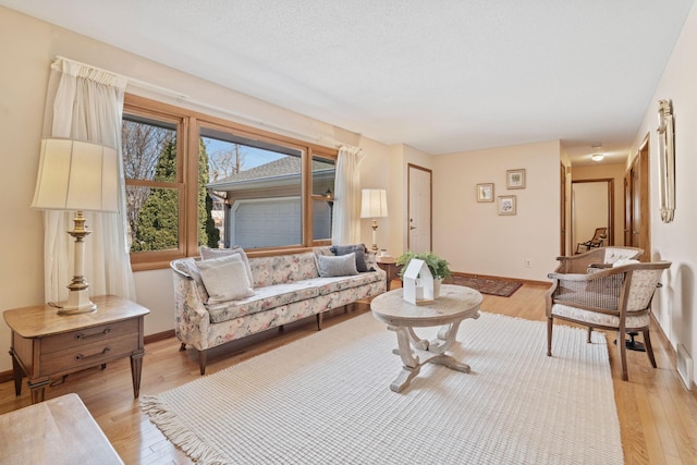 living area with a textured ceiling, baseboards, and light wood-style floors