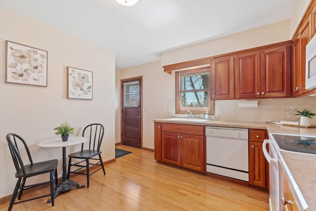 kitchen with white appliances, light wood finished floors, a sink, light countertops, and backsplash