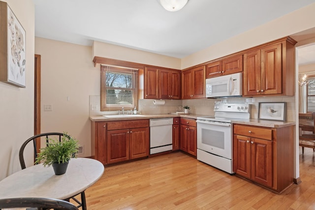 kitchen with light wood-type flooring, a sink, backsplash, white appliances, and brown cabinetry