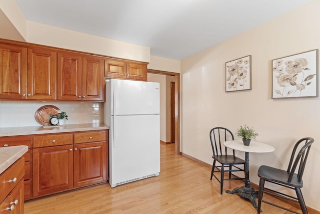 kitchen with brown cabinetry, decorative backsplash, light countertops, and freestanding refrigerator