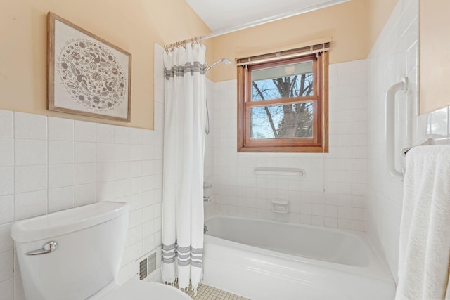 bathroom featuring visible vents, shower / bath combo with shower curtain, toilet, tile walls, and wainscoting