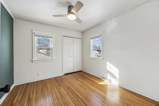 unfurnished bedroom featuring crown molding, a closet, ceiling fan, light wood-type flooring, and baseboards