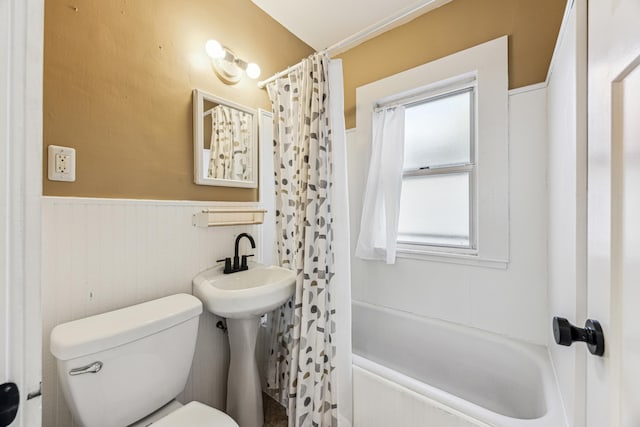 full bath with a wainscoted wall, shower / tub combo, and toilet