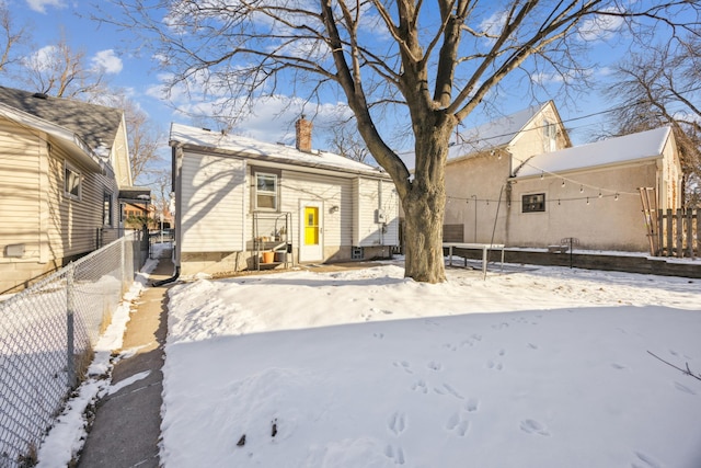 snow covered rear of property with a chimney and fence