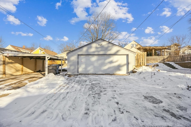 snow covered garage featuring a detached garage and fence