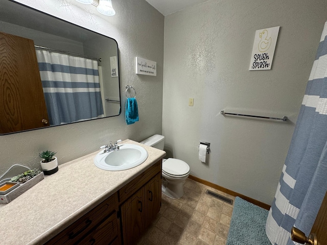 bathroom featuring a textured wall, toilet, vanity, visible vents, and baseboards