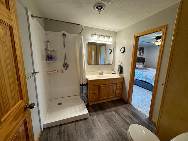 ensuite bathroom featuring visible vents, toilet, a stall shower, a textured ceiling, and wood finished floors