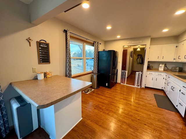 kitchen featuring recessed lighting, black fridge with ice dispenser, white cabinets, wood finished floors, and a peninsula