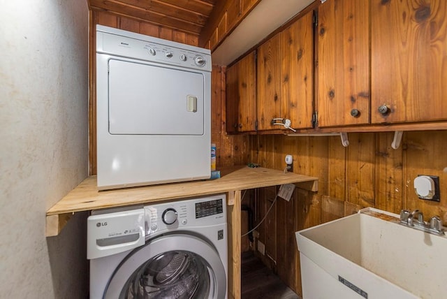 washroom featuring stacked washer / dryer, wooden walls, and a sink