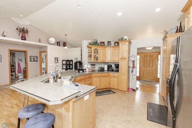 kitchen with a kitchen breakfast bar, light countertops, freestanding refrigerator, light brown cabinetry, and glass insert cabinets