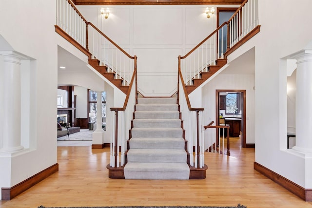 stairs with ornate columns, a decorative wall, wood finished floors, and a glass covered fireplace