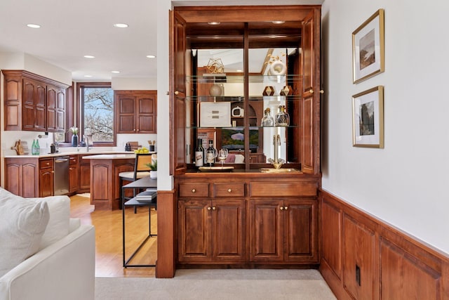 bar with light wood-style flooring, recessed lighting, stainless steel dishwasher, wainscoting, and a dry bar