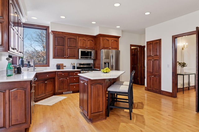 kitchen with appliances with stainless steel finishes, a center island, light countertops, light wood-type flooring, and a kitchen bar