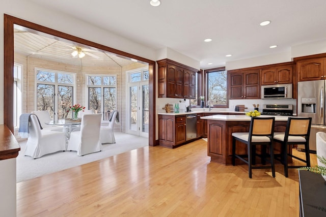 kitchen featuring stainless steel appliances, a sink, light countertops, a center island, and a kitchen bar