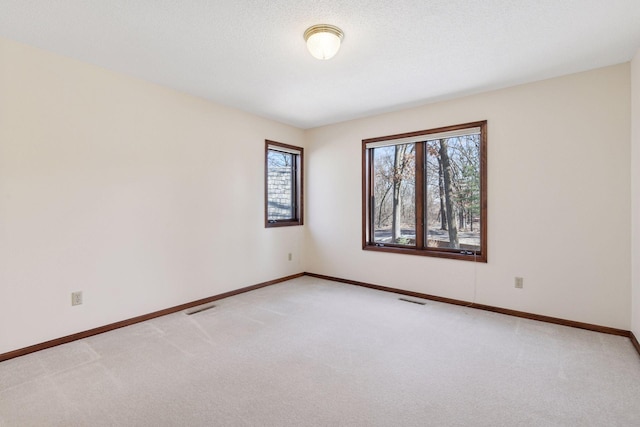 unfurnished room with baseboards, a textured ceiling, visible vents, and light colored carpet