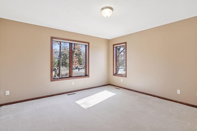 empty room featuring visible vents, light carpet, a wealth of natural light, and baseboards