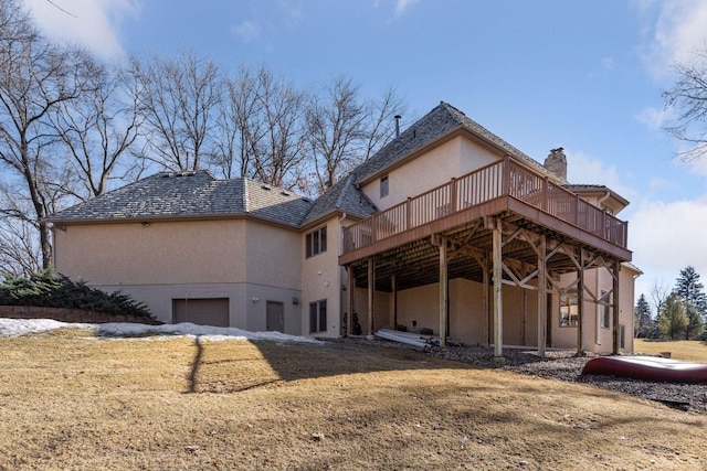 rear view of house with a chimney, an attached garage, a deck, a yard, and stucco siding