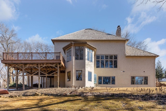 back of house with a chimney, a wooden deck, a lawn, and stucco siding