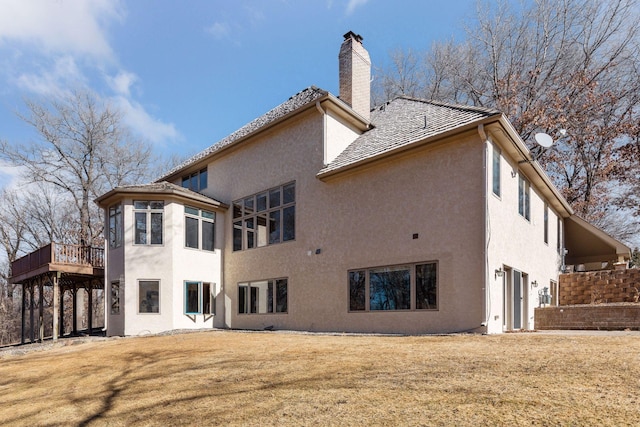 back of property featuring a deck, a yard, a chimney, and stucco siding