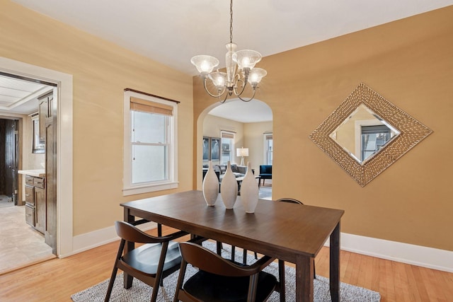 dining space featuring light wood-style floors, arched walkways, baseboards, and an inviting chandelier