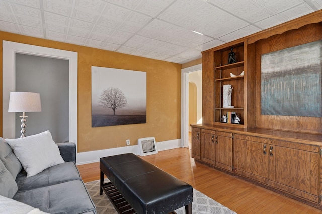 living area with built in features, arched walkways, visible vents, wood finished floors, and baseboards