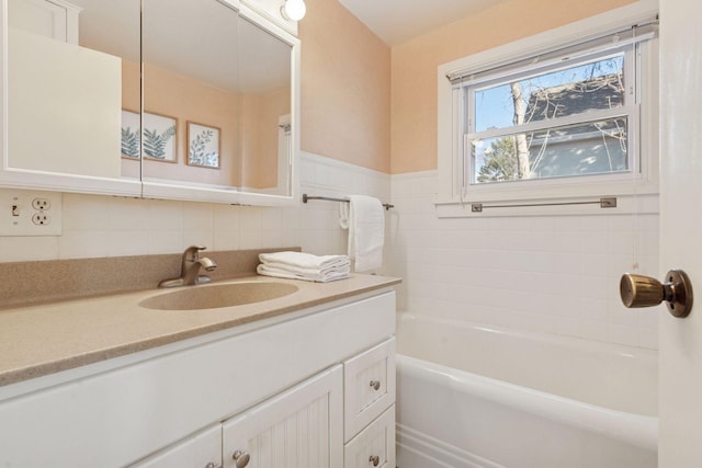 bathroom featuring a tub to relax in, wainscoting, vanity, and tile walls