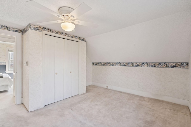 unfurnished bedroom featuring a ceiling fan, vaulted ceiling, a textured ceiling, carpet floors, and a closet