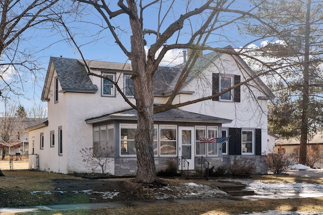 view of front of house featuring a shingled roof, fence, a sunroom, and stucco siding