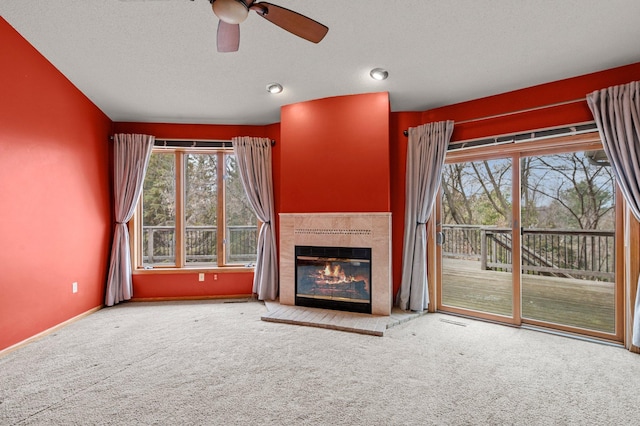 unfurnished living room featuring a ceiling fan, a textured ceiling, a tiled fireplace, carpet floors, and baseboards