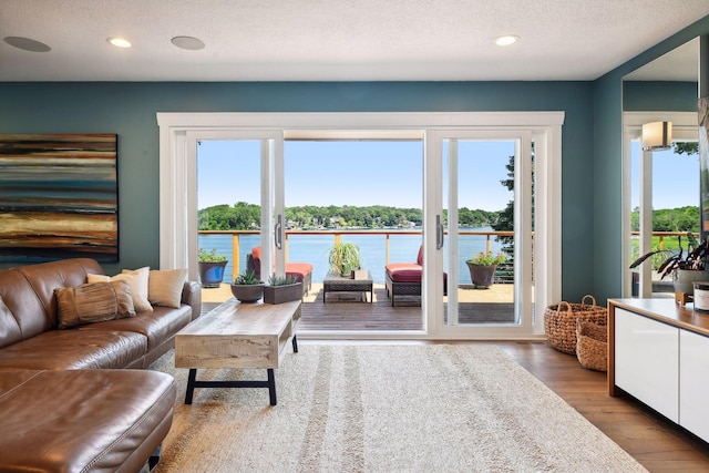 living area featuring a healthy amount of sunlight, a water view, a textured ceiling, and wood finished floors