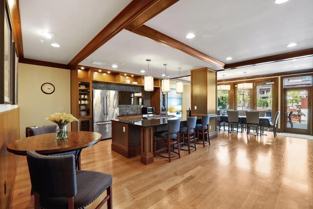 kitchen with light wood finished floors, decorative backsplash, stainless steel fridge, and a kitchen breakfast bar