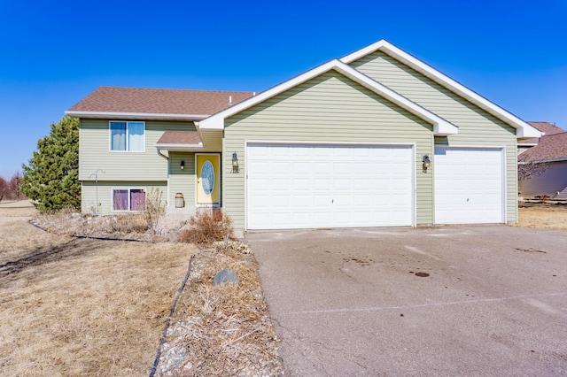 tri-level home with an attached garage, driveway, and roof with shingles