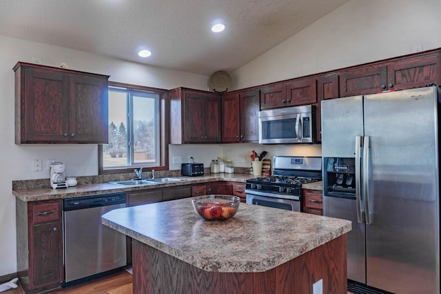 kitchen with lofted ceiling, a textured ceiling, stainless steel appliances, a kitchen island, and a sink