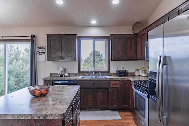 kitchen featuring a textured ceiling, dark brown cabinetry, stainless steel appliances, a sink, and light wood-type flooring