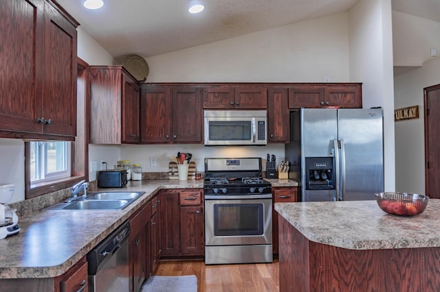 kitchen with vaulted ceiling, stainless steel appliances, light wood finished floors, and a sink