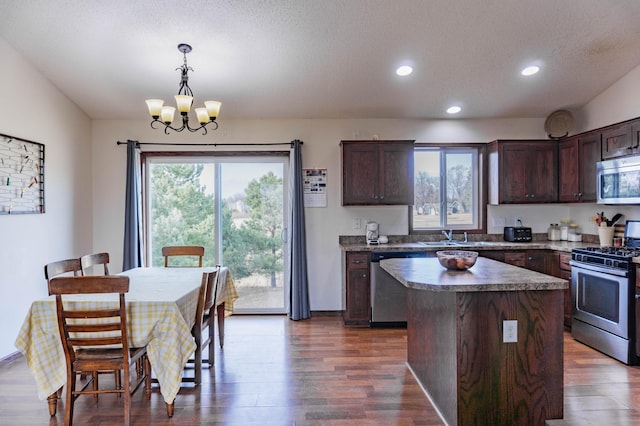 kitchen featuring dark brown cabinetry, dark wood finished floors, a center island, an inviting chandelier, and stainless steel appliances