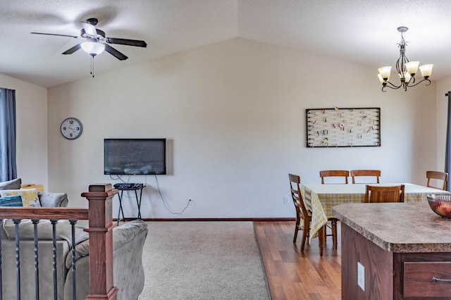 dining space featuring ceiling fan with notable chandelier, vaulted ceiling, baseboards, and wood finished floors