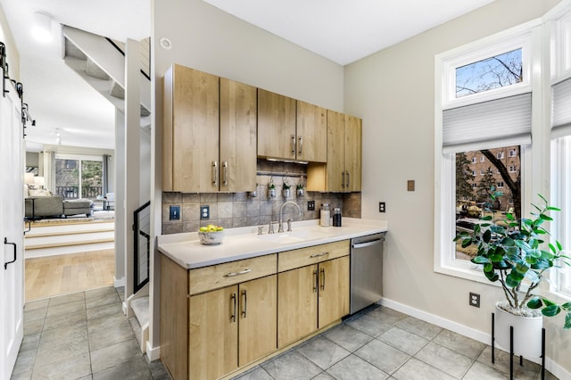 kitchen featuring light countertops, backsplash, stainless steel dishwasher, a barn door, and a sink