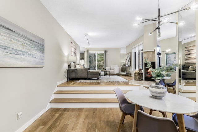 dining area featuring an inviting chandelier, track lighting, wood finished floors, a tile fireplace, and baseboards