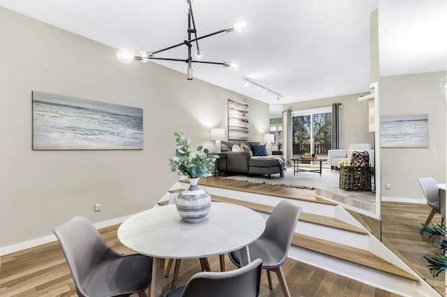 dining space with rail lighting, baseboards, a chandelier, and wood finished floors