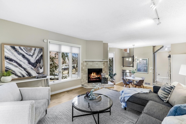 living room with baseboards, a tiled fireplace, visible vents, and light wood-style floors