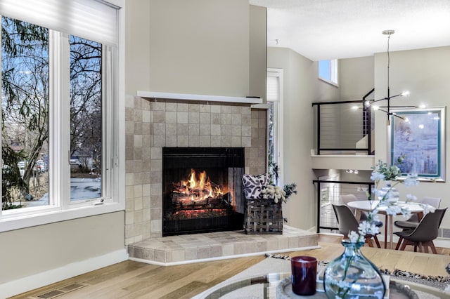 living area with a chandelier, a tile fireplace, wood finished floors, visible vents, and baseboards