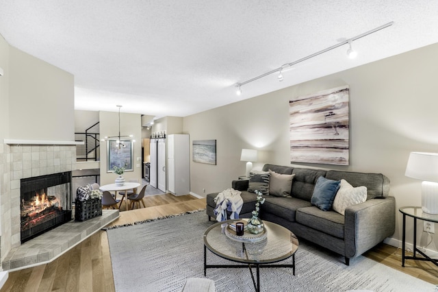 living room with a textured ceiling, light wood finished floors, a tile fireplace, and baseboards